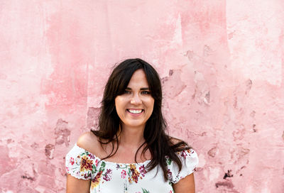 Portrait of smiling woman standing against pink wall