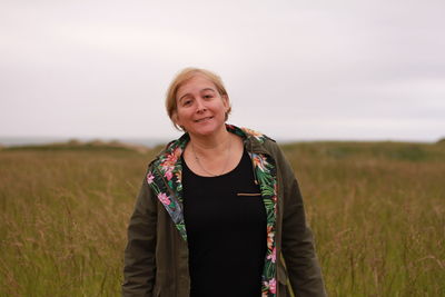 Portrait of smiling young woman standing on field against sky