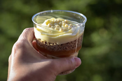 Sweet dessert trifle in transparent glass in woman's hand against green background. copy space.