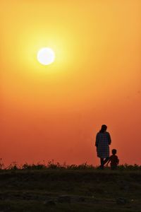Rear view of silhouette man standing on field against orange sky