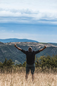 Rear view of man with arms outstretched standing against sky