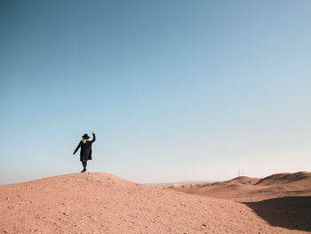 Unrecognized woman standing and dancing on sand dune against clear sky