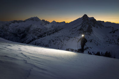 Man with headlamp walking on snowy mountain at sunset