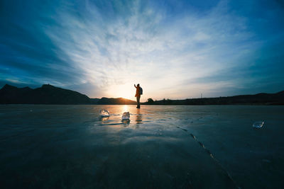 Rear view of man standing on frozen landscape against sky during sunset