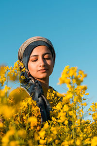 Young woman by yellow flowering plants against clear sky