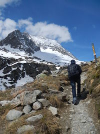 Rear view of man walking on trail by mountain against sky during winter