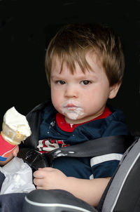 Messy toddler with ice cream cone sitting in his car seat