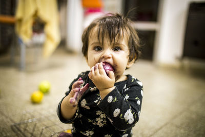 Portrait of cute messy baby girl eating food while sitting on floor at home