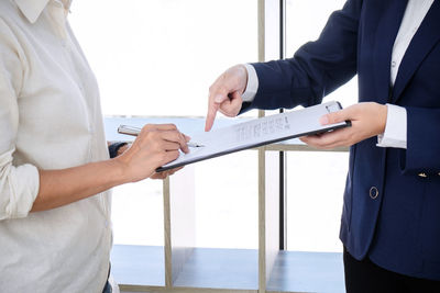 Midsection of woman signing on paper held by businessman in office
