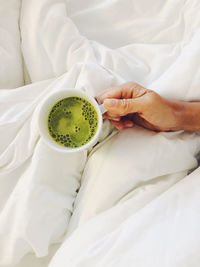 Directly above shot of cropped hand of man holding green tea on bed