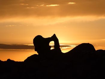 Silhouette man on rock against sky during sunset