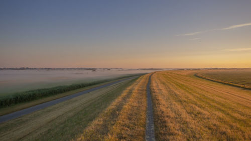 Road passing through field against sky during sunset