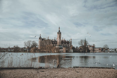 Buildings by river against cloudy sky