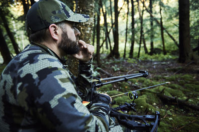 Side view of young man holding camera in forest