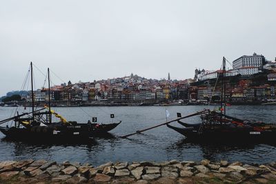 Sailboats moored on river by buildings against sky