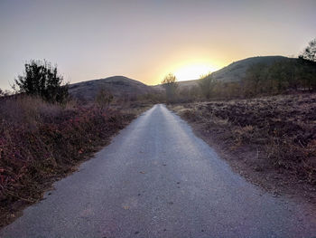 Empty road along landscape at sunset