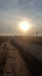 Surface level of road leading towards field against cloudy sky during sunset