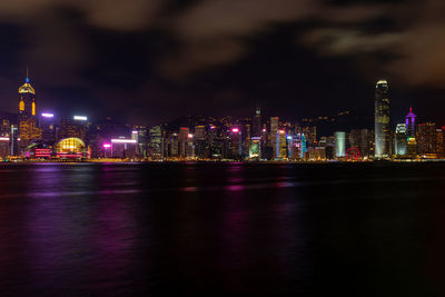 Illuminated buildings by river against sky at night