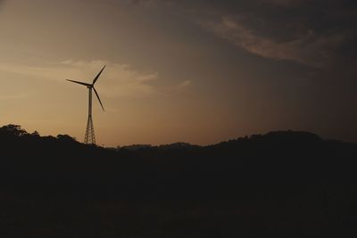 Silhouette of wind turbines on field against sky during sunset