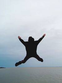 Teenage boy jumping at beach against sky
