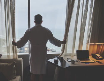 Rear view of man looking through window