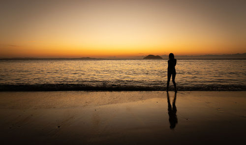 Silhouette woman standing at beach against sky during sunset