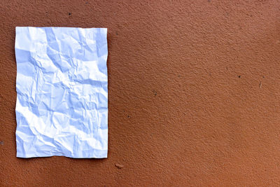 Close-up of blank crumpled paper stuck on brown wall
