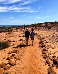 Rear view of boys walking at beach against sky