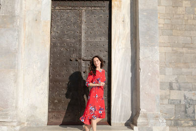 Portrait of woman standing by metallic door against brick wall