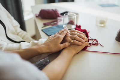 Cropped image of female caregiver stacking hands on senior woman at retirement home