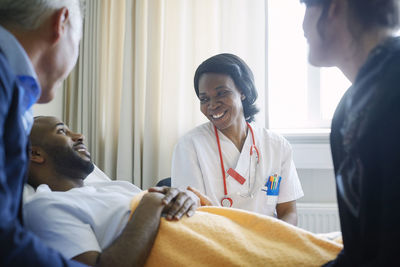 Smiling female doctor talking to patient and family in hospital ward