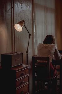 Rear view of woman sitting on table at home