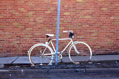 Obsolete bicycle parked on footpath against brick wall