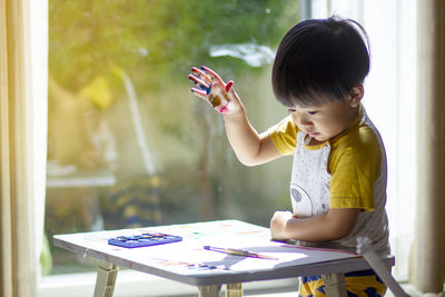 Girl holding table while standing by window