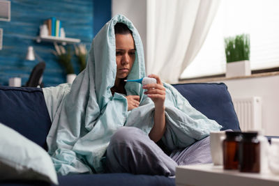 Sick woman checking temperature sitting at home