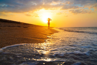 Rear view of man walking at beach against sky during sunset