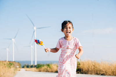 Portrait of smiling young woman with arms raised standing against sky