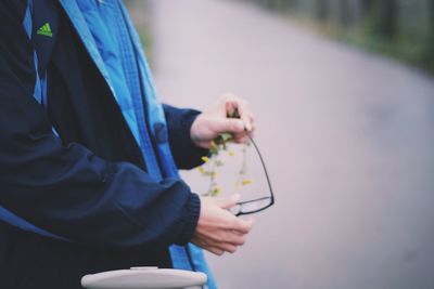 Midsection of man holding eyeglasses and flowers on road