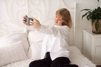 Portrait of young woman using mobile phone while sitting on bed at home