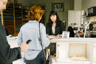 Technician discussing with female customer over damaged laptop at repair shop