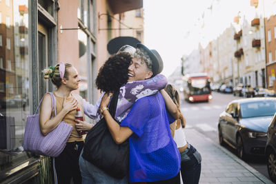 Happy young man with eyes closed hugging female friend in city