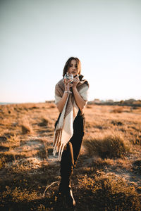 Full length of young woman standing on field against clear sky