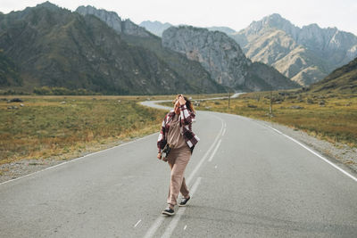 Young woman on skateboard on road against the beautiful mountain landscape, chemalskiy tract, altai