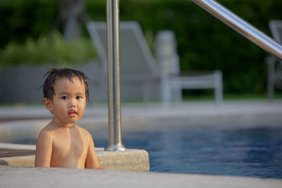 Portrait of shirtless boy sitting in swimming pool