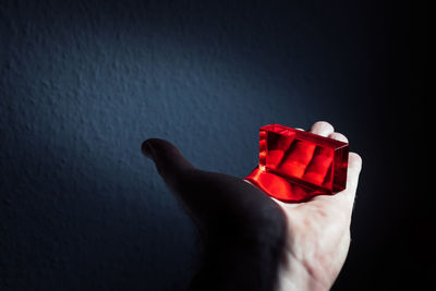 Cropped hand holding red glass slab against wall