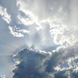 Low angle view of sunlight streaming through clouds