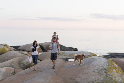 Woman looking at man carrying girl on shoulder walking against sky