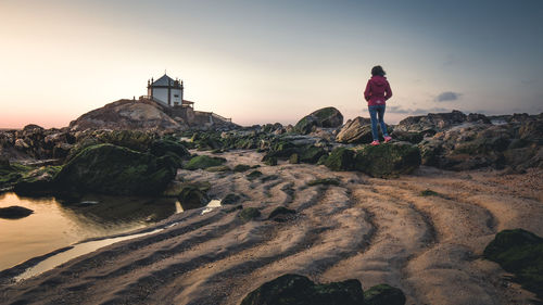 Rear view of woman standing on rock at beach against sky