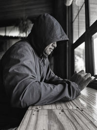 A man is acting suspiciously, wearing a concealed hood and long-sleeved shirt, playing on his mobile