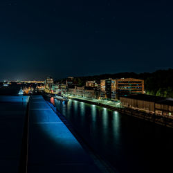 Illuminated bridge over river by buildings against sky at night